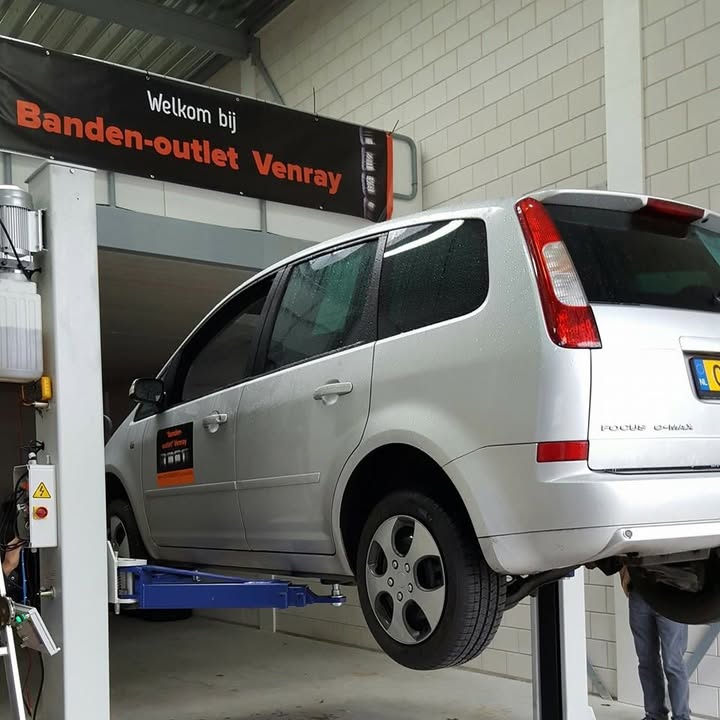 Welkom bij Banden-outlet Venray: auto op de hefbrug onder het welkomstbord