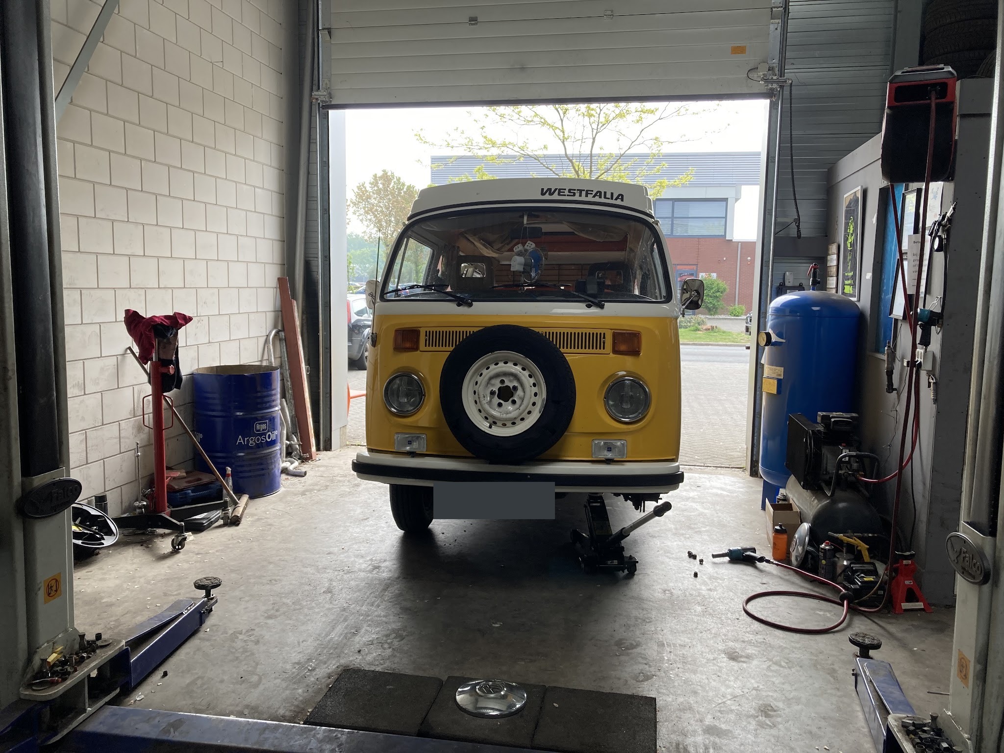 Gele Volkswagen T2 bus op de hefbrug bij de open roldeur