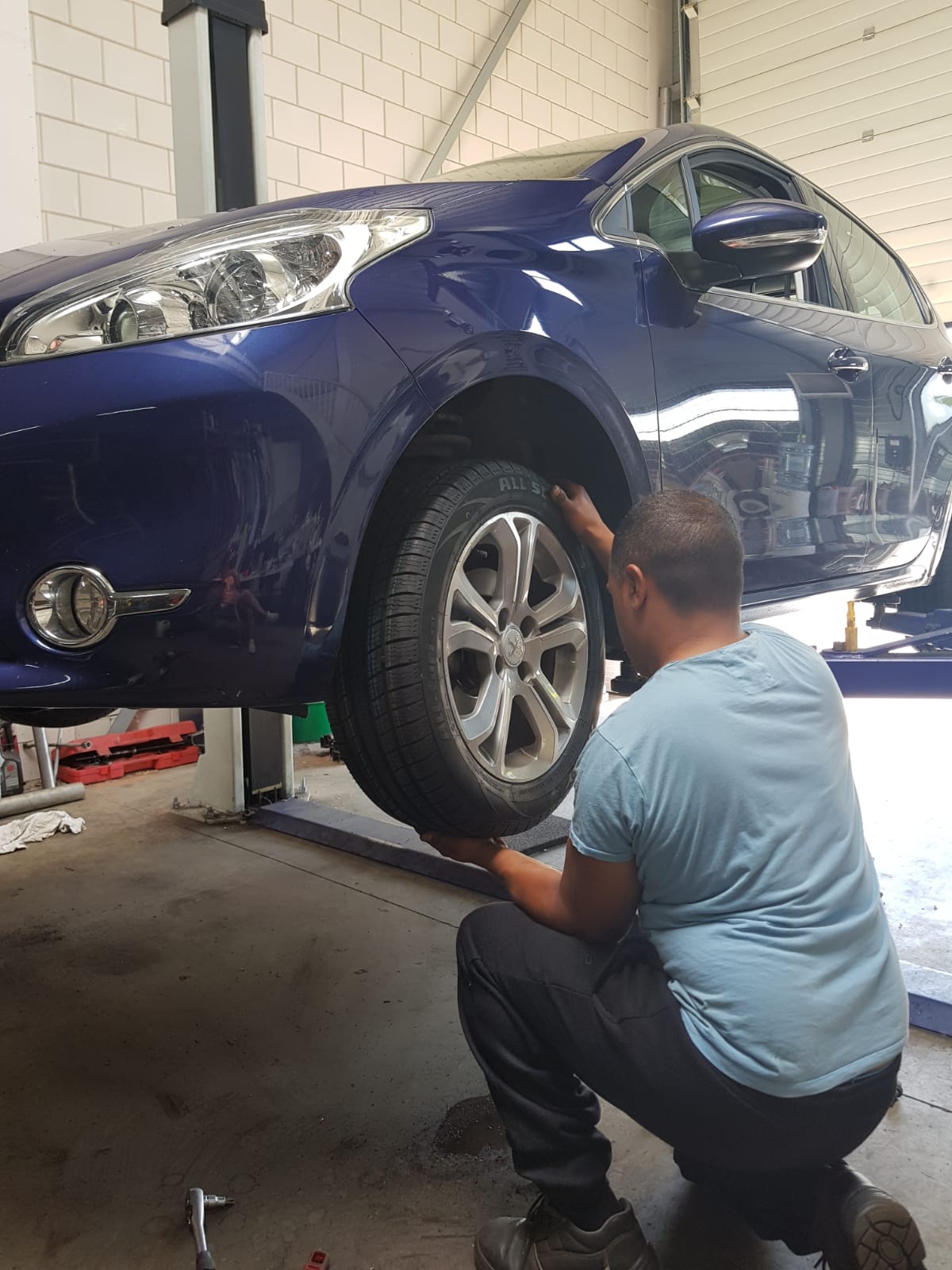 Monteur monteert een wiel op een blauwe Peugeot op de hefbrug