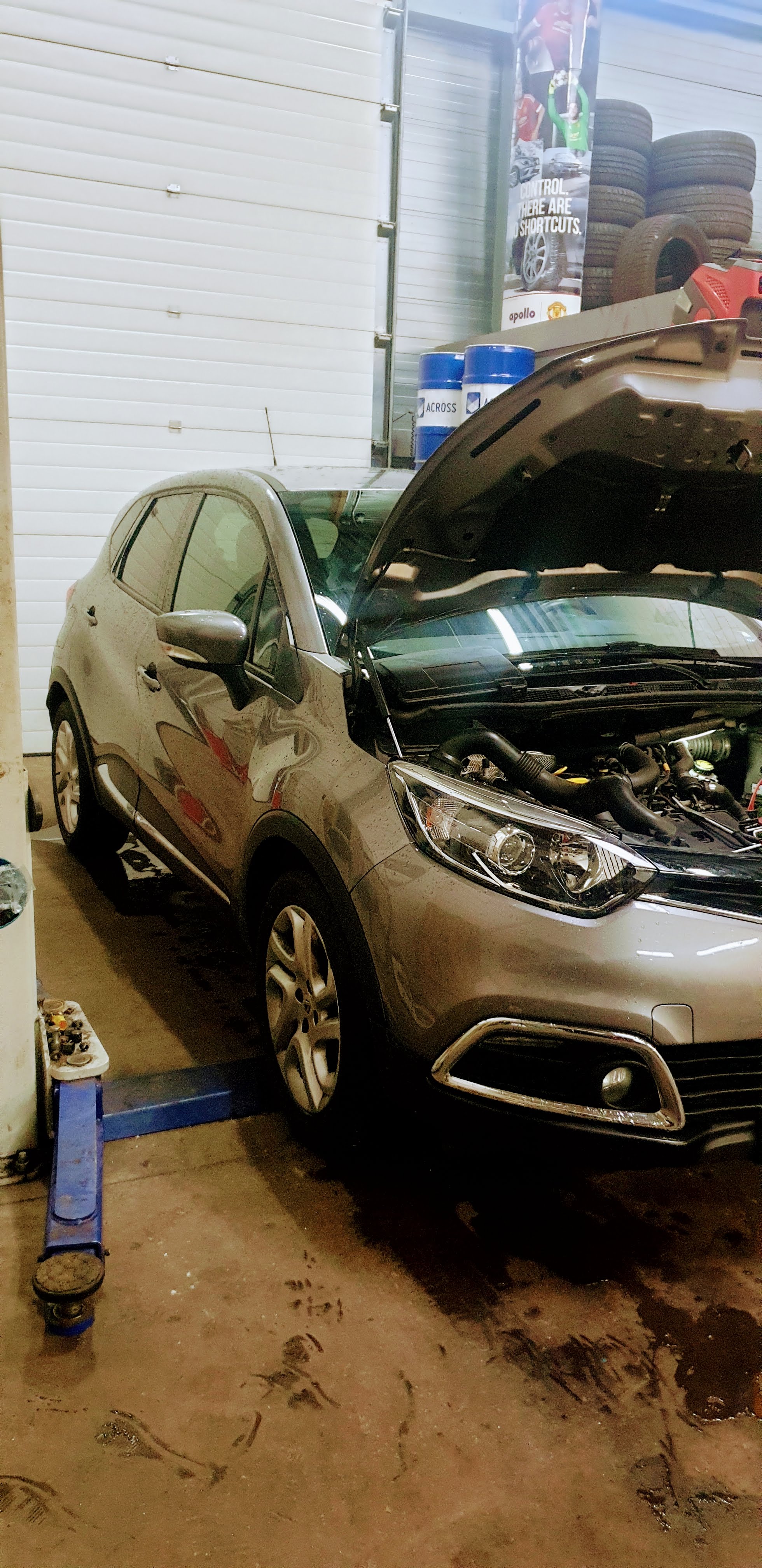 Grijze Renault Captur met open motorkap in de werkplaats, bandenrek op de achtergrond